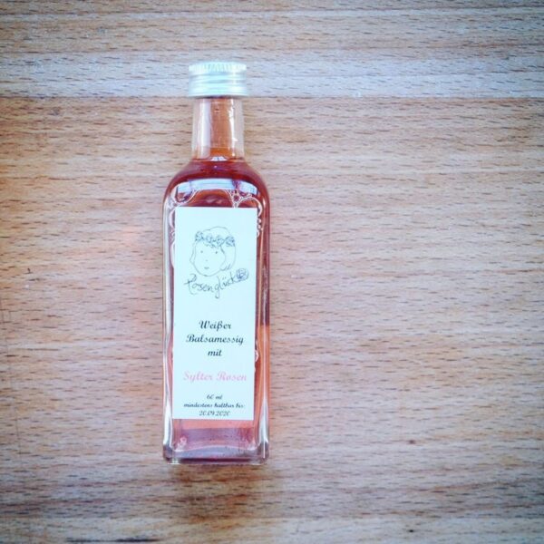 92515022_212054293388782_5489653651473604141_n-2.jpg Eine 100ml SYLTER ROSEN BALSAMESSIG-Flasche mit Rosenbalsamico-Essig-Etikett steht elegant auf einer Holzoberfläche.