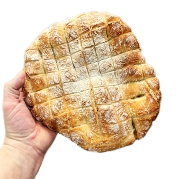 Eine Hand hält einen runden Laib BIO DINKEL FONDUE BROT, der eine knusprige Oberfläche mit einem Kreuzmuster aufweist.