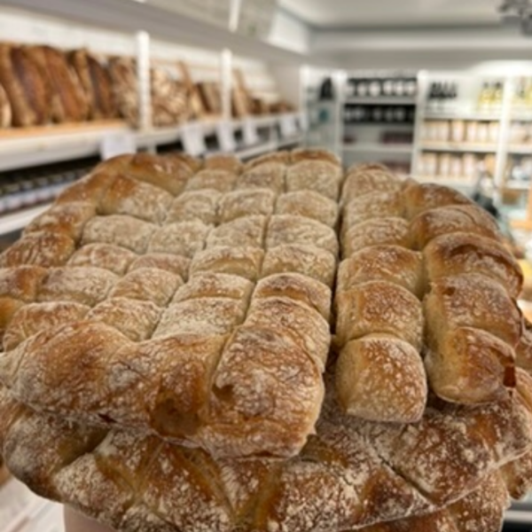 Fonduebrot Dinkel Lund sylt Nahaufnahme von frischen BIO DINKEL FONDUE BROT-Broten mit bemehlter Kruste, ausgestellt in einer Bäckerei mit Regalen voller Brot im Hintergrund.