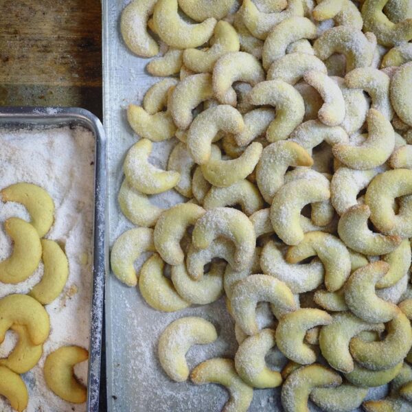 Lund-sylt-vanille-Kipfel-Vanillekipferl-rezept-suedspitze-1.jpg Mit Zucker bestäubte Tahiti-Vanille-Kipfel auf einem Backblech neben mit Puderzucker überzogenen Kipfeln.