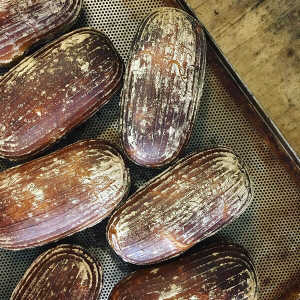 Roggenmischbrot_Wittenberger_Sylt_Bio_Brot_steinofen_rustikal_sourdough-3-3.jpg Eine Schale BIO MISCHBROT 500g, frisch gebackenes rustikales Brot mit goldbrauner Kruste auf einem perforierten Backblech.