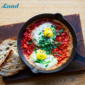 TOFREE NORTH SHAKSHUKA, serviert mit zwei Eiern, grüner Garnitur und Sauerteigbrot auf einem Holzbrett.