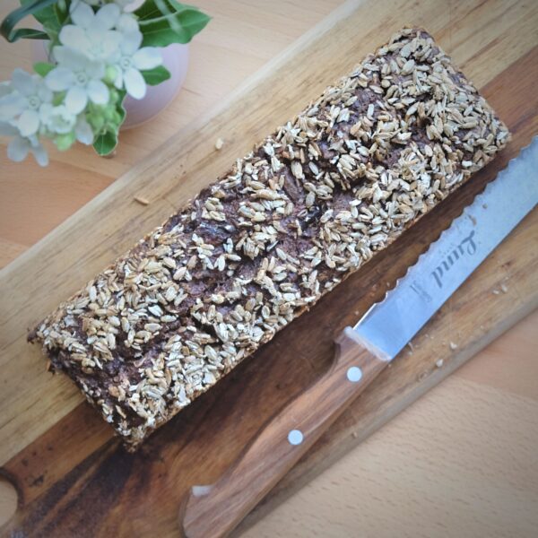 Walnuss-Stange-Friesen-Voillkornbrot-Lund-Sylt-Sauerteig-2-5.jpg Ein BIO SONNEN-BLUMEN-STANGE-Laib und ein Messer liegen elegant auf dem Schneidebrett und laden dazu ein, die gesunde Kruste zu zerschneiden.